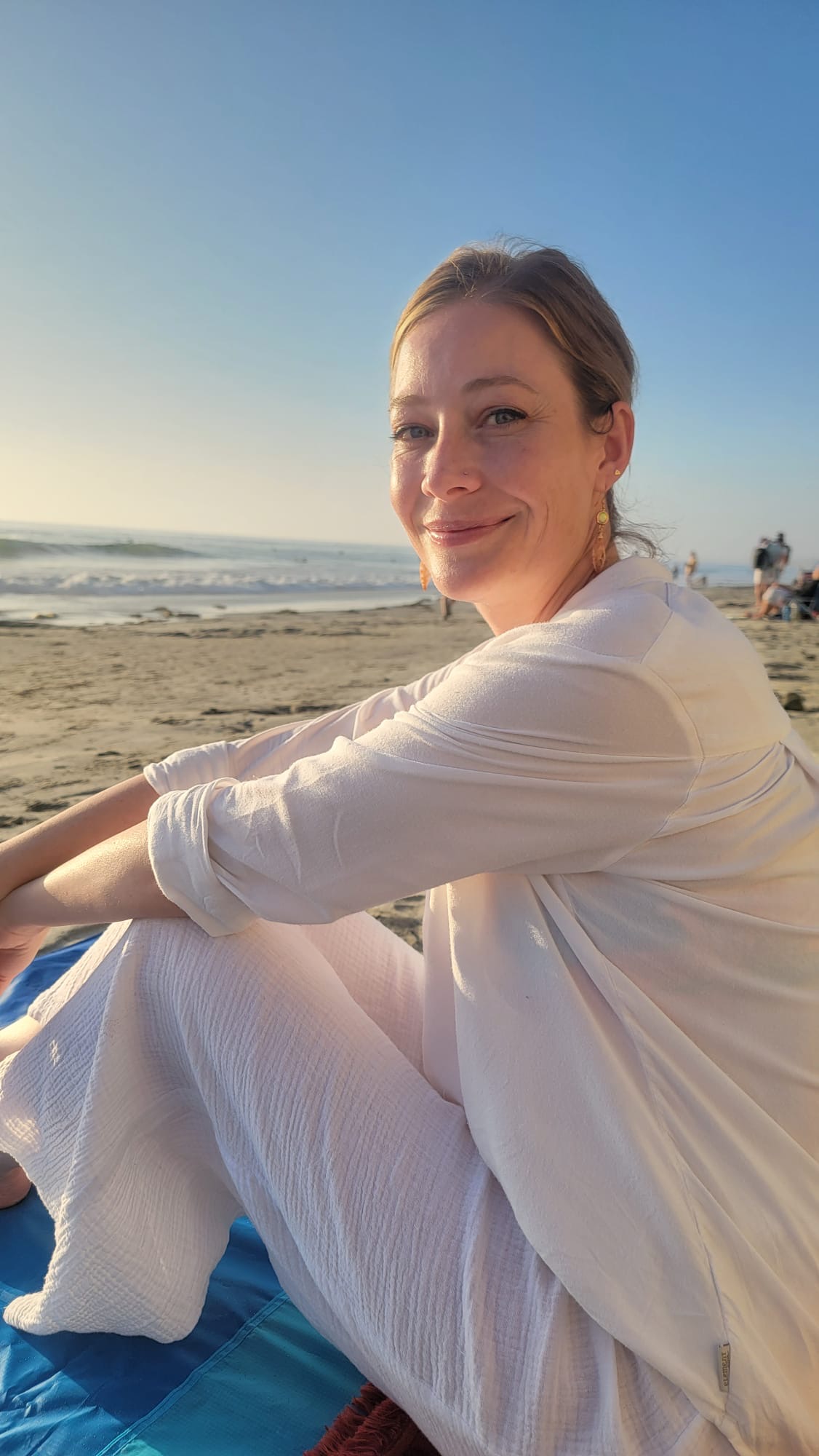 Dr. Brittany Rice, PhD, somatic practitioner and clinical psychologist, walking along the shoreline in flowing white linen at golden hour