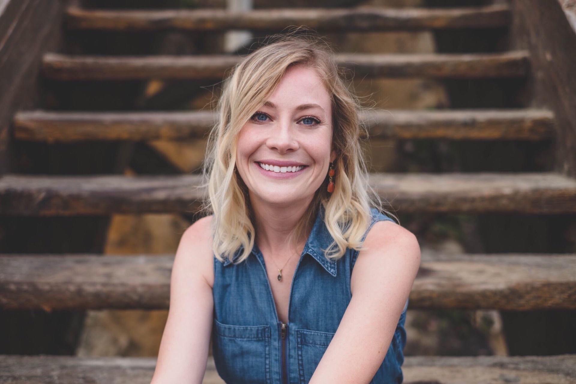 Warm portrait of Dr. Brittany Rice, PhD, smiling on wooden steps in a denim dress, welcoming new clients to reach out