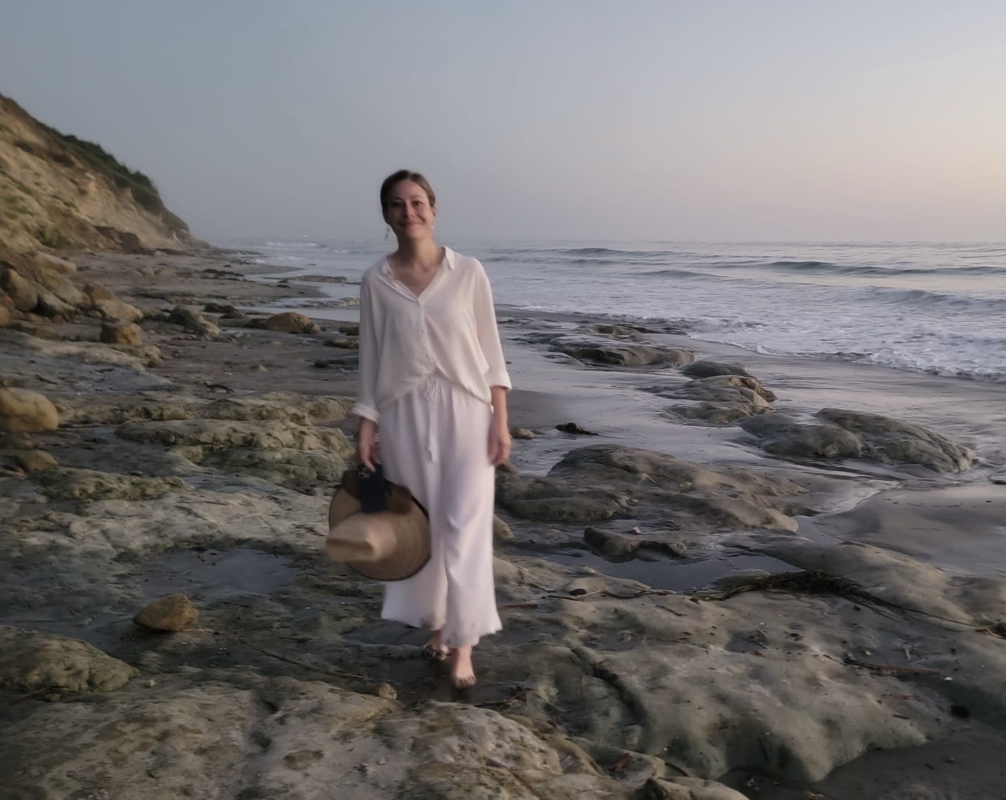 Dr. Brittany Rice, PhD, somatic practitioner and clinical psychologist, walking barefoot along a rocky Pacific shoreline at golden hour